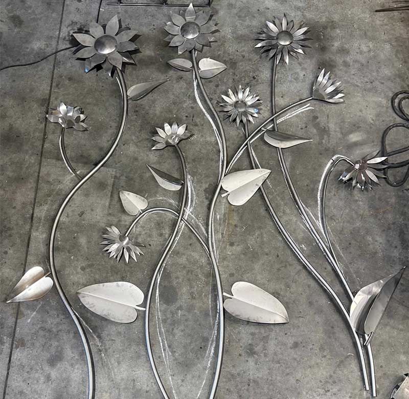 overview of a monumental stainless steel wall sculpture laid out on the workshop floor with chalk lines